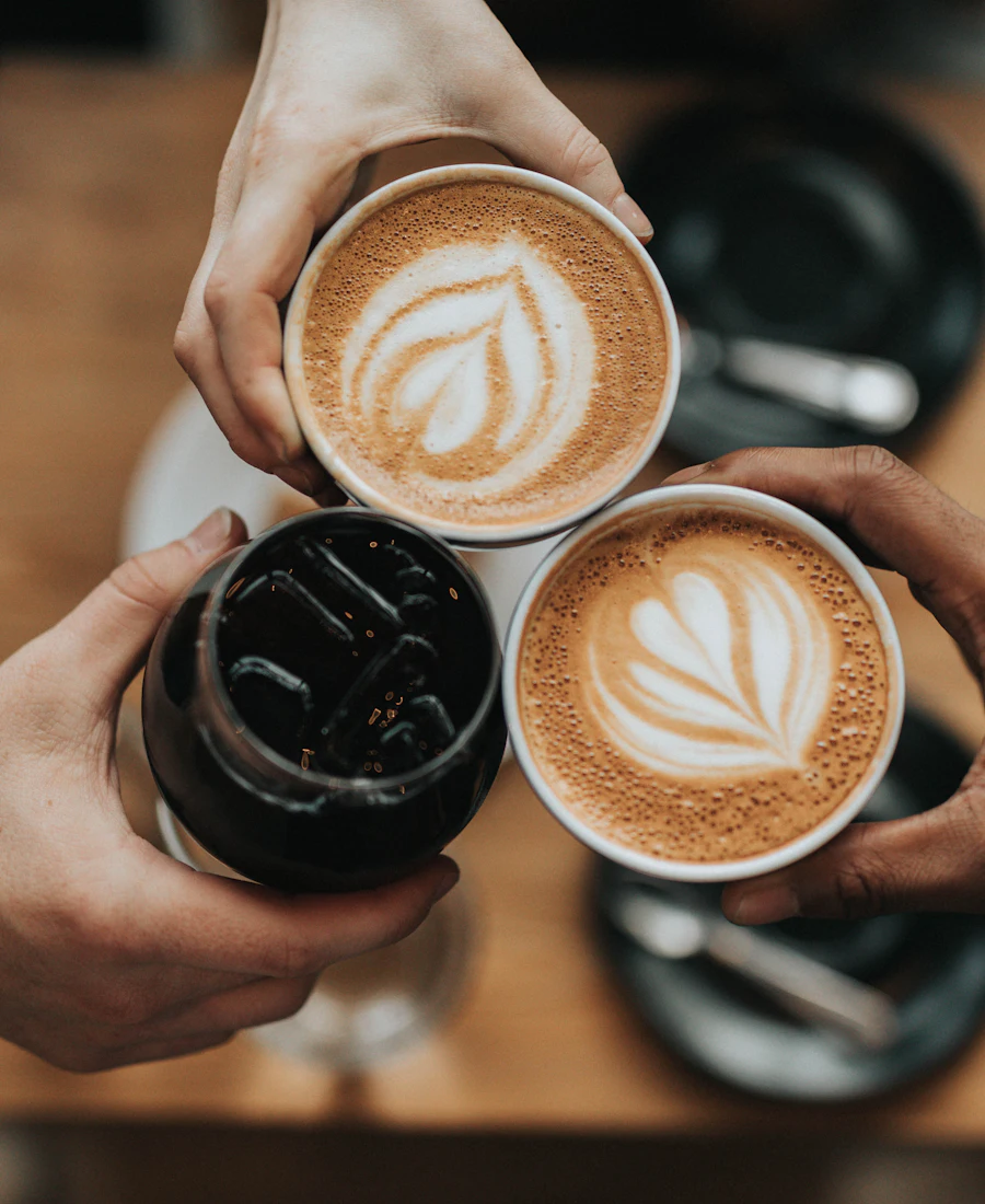 Two people holding cups of latte with latte art over a wooden table